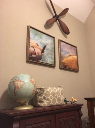A replica of a vintage propeller creates a nice focal point, which will eventually be centered above the "big boy" bed when transitioned out of the crib. Two prints of vintage planes add a touch of color and coordinate well with the vintage globe (from Mom's childhood). The furniture piece was purchased and replainted from Goodwill and provides lots fo storage for extra linens (crib sheets, waterproof mattress pads and blankets).